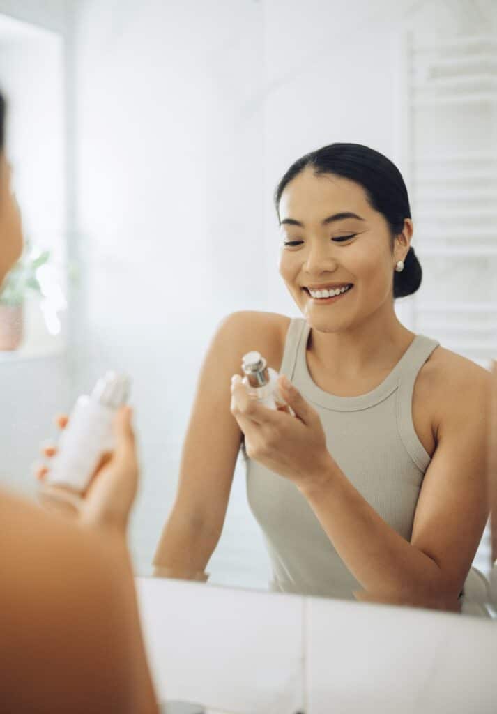a woman putting on a skin care product in the mirror